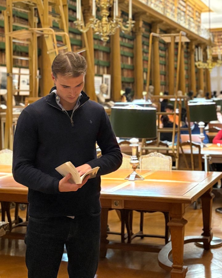 Guillaume, dans une bibliothèque, un livre à la main